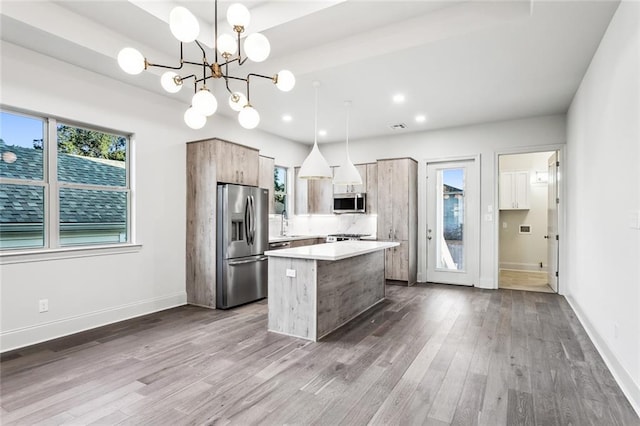 kitchen featuring appliances with stainless steel finishes, decorative light fixtures, a kitchen island, and wood-type flooring