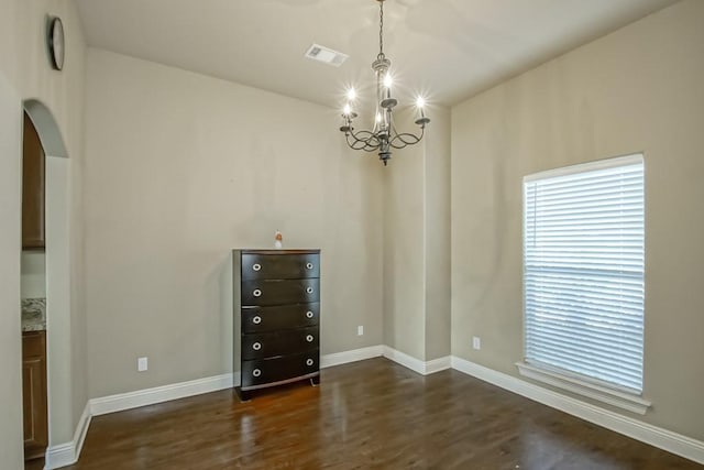 unfurnished room featuring dark wood-type flooring and an inviting chandelier