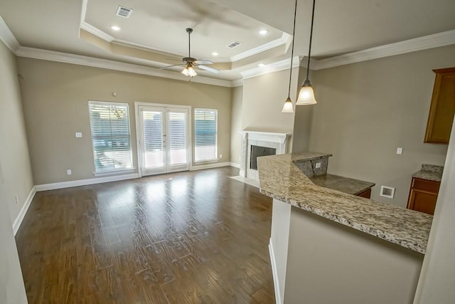 unfurnished living room with a tray ceiling, ceiling fan, dark wood-type flooring, and ornamental molding