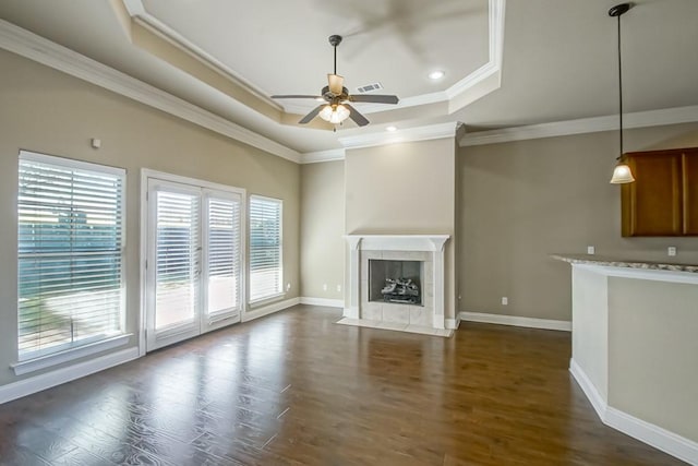 unfurnished living room featuring a tile fireplace, crown molding, dark hardwood / wood-style floors, ceiling fan, and a tray ceiling