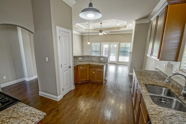 kitchen featuring a tray ceiling, ceiling fan, dark wood-type flooring, sink, and pendant lighting