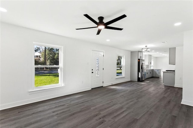 unfurnished living room featuring ceiling fan with notable chandelier and dark hardwood / wood-style floors