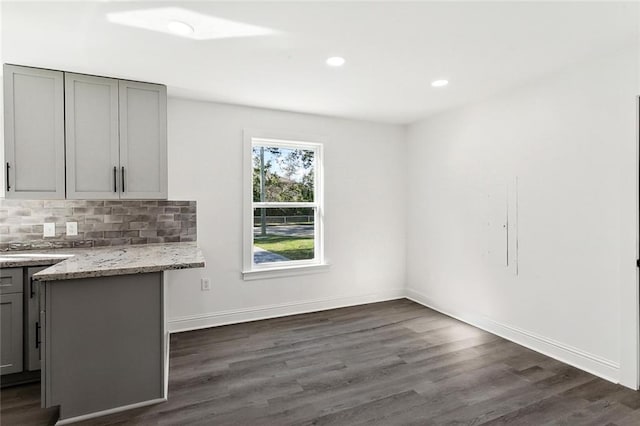 kitchen featuring backsplash, gray cabinets, light stone counters, and dark wood-type flooring