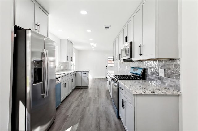 kitchen featuring tasteful backsplash, light hardwood / wood-style floors, light stone counters, white cabinetry, and stainless steel appliances