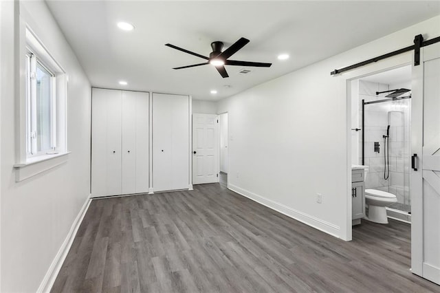 unfurnished bedroom featuring ensuite bathroom, a barn door, light hardwood / wood-style floors, and ceiling fan