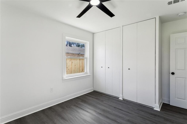 unfurnished bedroom featuring ceiling fan, dark hardwood / wood-style flooring, and two closets