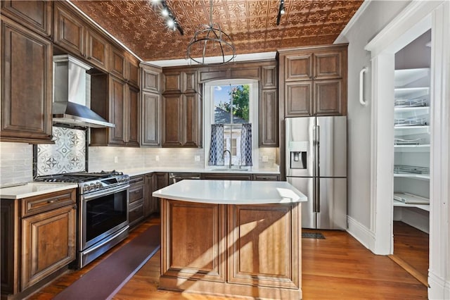 kitchen featuring a center island, wall chimney range hood, sink, stainless steel appliances, and brick ceiling