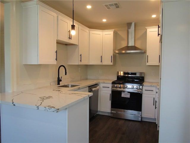 kitchen featuring appliances with stainless steel finishes, white cabinets, wall chimney exhaust hood, sink, and kitchen peninsula