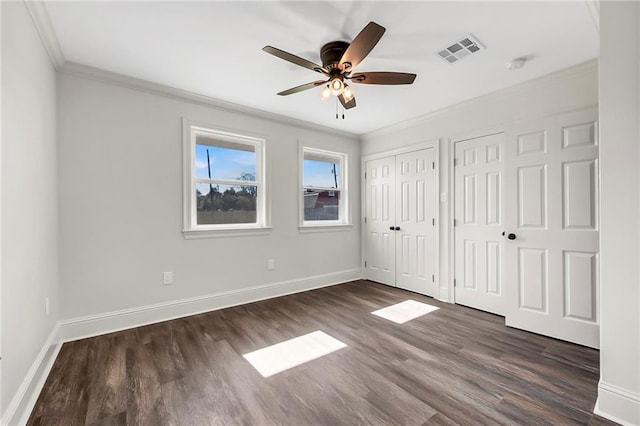 unfurnished bedroom featuring ceiling fan, dark hardwood / wood-style flooring, crown molding, and multiple closets