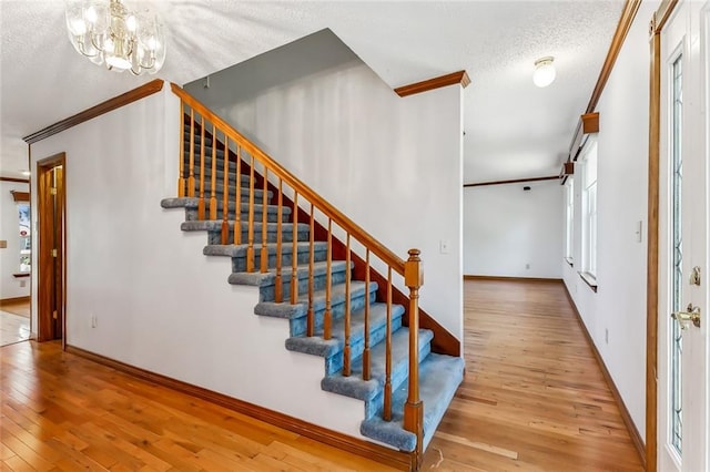 stairs with a chandelier, a textured ceiling, hardwood / wood-style flooring, and crown molding