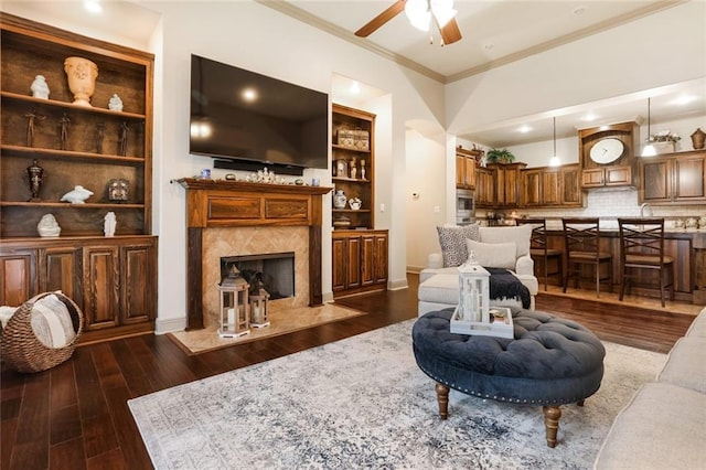 living room with built in shelves, ceiling fan, dark hardwood / wood-style flooring, a fireplace, and ornamental molding