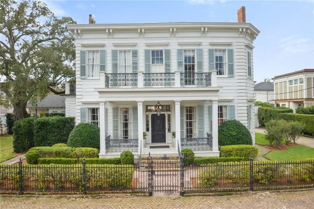 view of front of house featuring a balcony, a fenced front yard, and a chimney