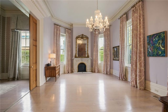 unfurnished living room featuring light wood-type flooring, a healthy amount of sunlight, crown molding, and an inviting chandelier