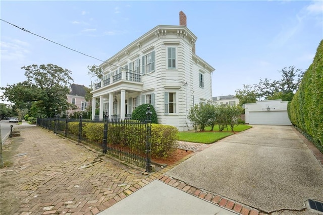 italianate-style house featuring a fenced front yard, a chimney, a detached garage, and a balcony