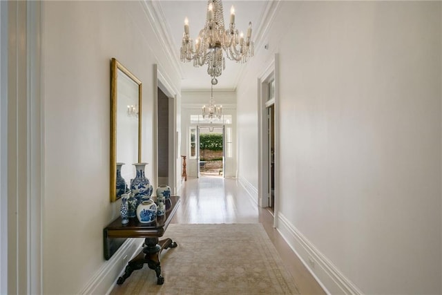 corridor with crown molding, baseboards, and an inviting chandelier