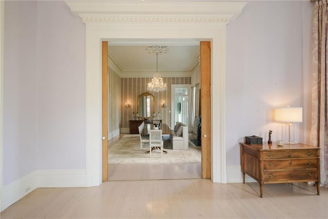 hallway featuring light wood-style floors, crown molding, baseboards, and a notable chandelier