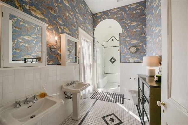 full bath with two sinks, tile patterned flooring, toilet, wainscoting, and wallpapered walls