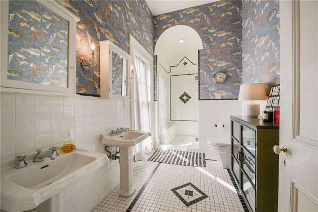 bathroom with tile walls, wallpapered walls, toilet, a sink, and tile patterned floors