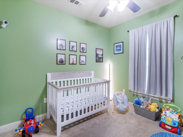 carpeted bedroom featuring ceiling fan and a nursery area