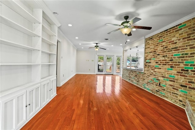 unfurnished living room featuring french doors, ornamental molding, brick wall, ceiling fan with notable chandelier, and hardwood / wood-style floors