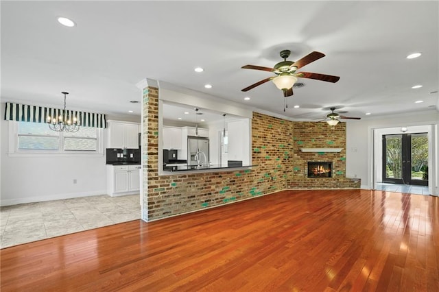 136 Rebel Ave, River Ridge, LA 70123 - unfurnished living room with a chandelier, ceiling fan, light wood-style flooring, a brick fireplace, and recessed lighting