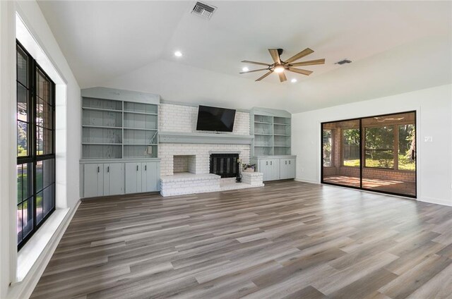 unfurnished living room with a brick fireplace, vaulted ceiling, ceiling fan, hardwood / wood-style flooring, and built in features