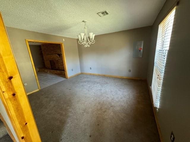 spare room with dark colored carpet, a notable chandelier, electric panel, a textured ceiling, and a fireplace