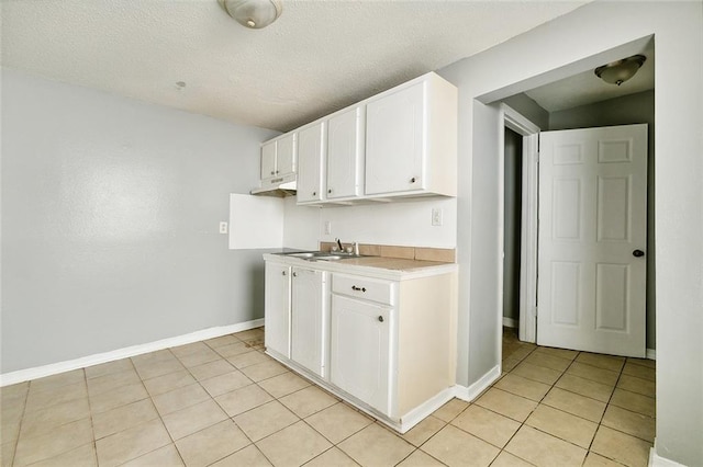 kitchen featuring a textured ceiling, sink, white cabinets, and light tile patterned floors