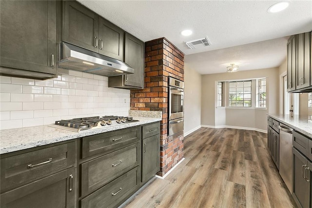 kitchen with tasteful backsplash, light stone counters, a textured ceiling, stainless steel appliances, and light hardwood / wood-style floors