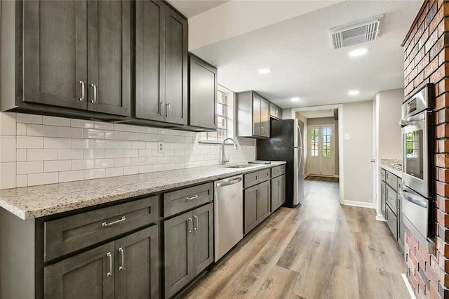 kitchen with sink, decorative backsplash, light wood-type flooring, light stone counters, and stainless steel appliances