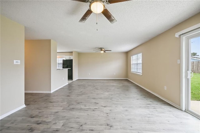 unfurnished living room with a textured ceiling, light wood-type flooring, ceiling fan, and a healthy amount of sunlight