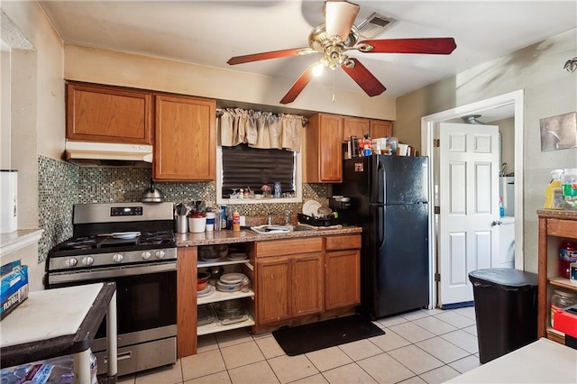 kitchen with stainless steel gas stove, sink, tasteful backsplash, black fridge, and light tile patterned floors