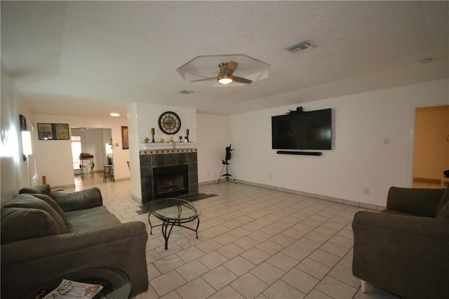 living room featuring a tiled fireplace, ceiling fan, light tile patterned floors, and a textured ceiling