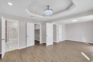 unfurnished bedroom with dark hardwood / wood-style floors, a tray ceiling, and ensuite bath