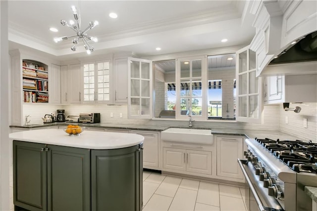 kitchen with white cabinets, a raised ceiling, sink, high end stainless steel range oven, and tasteful backsplash