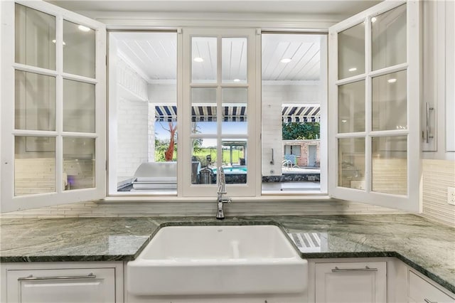 kitchen with tasteful backsplash, white cabinetry, dark stone countertops, and sink