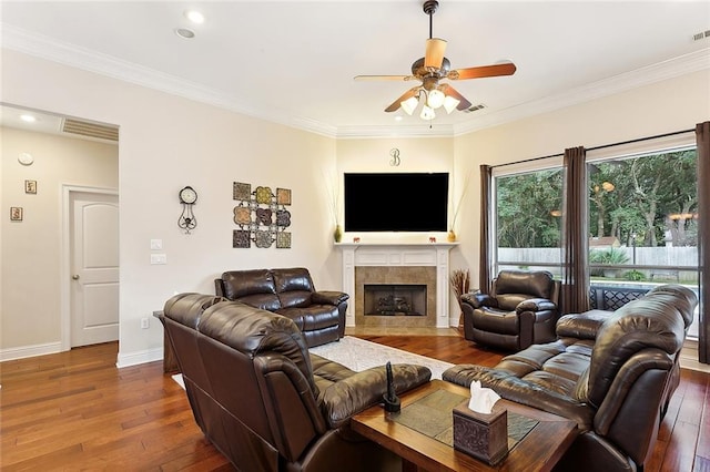 living room featuring a tile fireplace, wood-type flooring, ceiling fan, and crown molding