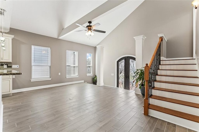 unfurnished living room featuring decorative columns, arched walkways, stairway, wood finished floors, and french doors