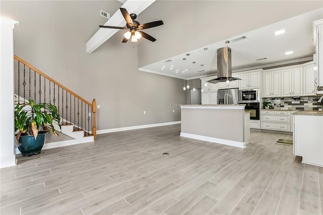 kitchen featuring a ceiling fan, island range hood, visible vents, stainless steel fridge with ice dispenser, and oven