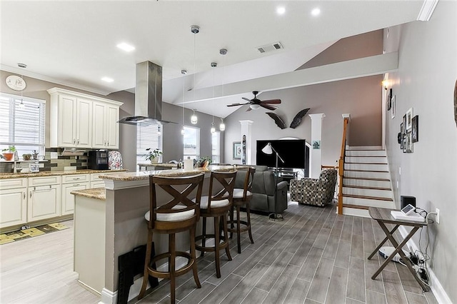 kitchen featuring island range hood, open floor plan, hanging light fixtures, light stone countertops, and a kitchen bar