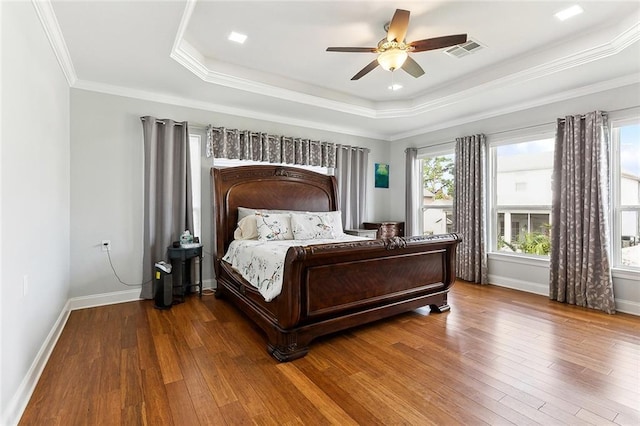bedroom with visible vents, crown molding, hardwood / wood-style floors, baseboards, and a tray ceiling
