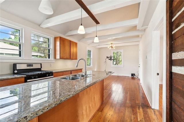 kitchen featuring pendant lighting, stone counters, stainless steel range with gas cooktop, sink, and beamed ceiling