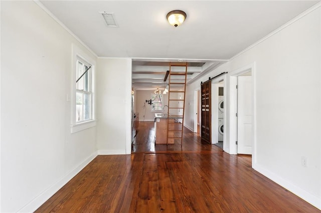 spare room featuring a barn door, crown molding, stacked washer and dryer, and dark wood-type flooring