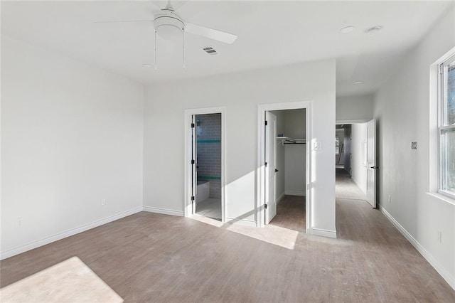 unfurnished bedroom with ensuite bath, light hardwood / wood-style flooring, ceiling fan, a spacious closet, and a closet