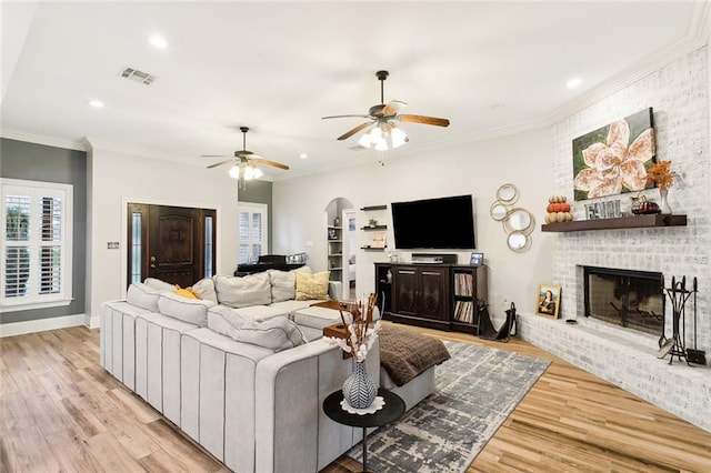 living room featuring a fireplace, ceiling fan, crown molding, and light hardwood / wood-style flooring