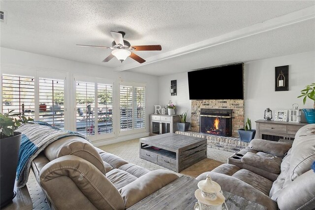 living room featuring ceiling fan, a fireplace, and a textured ceiling