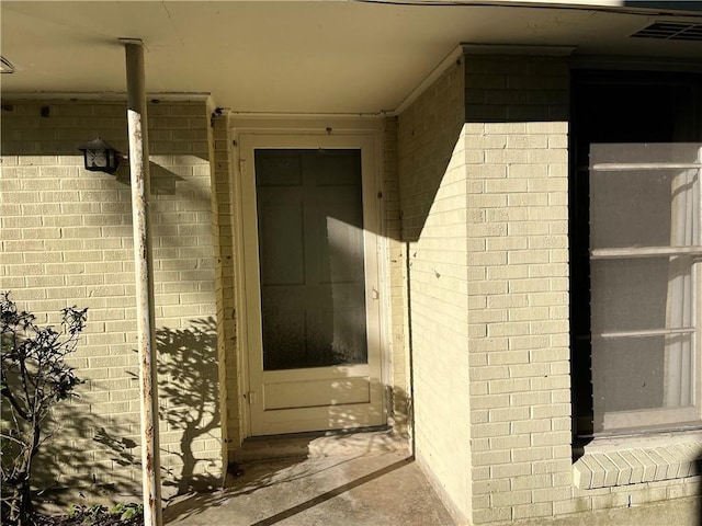 view of exterior entry featuring brick siding and visible vents