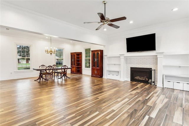 living room with a fireplace, wood-type flooring, ceiling fan with notable chandelier, and ornamental molding