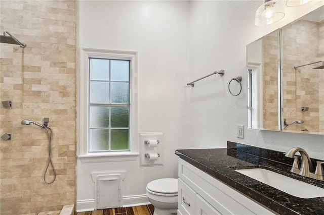 bathroom with hardwood / wood-style flooring, vanity, toilet, and tiled shower