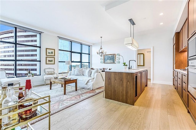 kitchen featuring sink, an inviting chandelier, light hardwood / wood-style flooring, pendant lighting, and a center island with sink